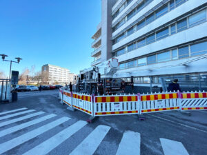 Kelta-puna-valkoinen suoja-aita ympäröi nostolava-autoa, joka seisoo Tyks-sairaalan vieressä.