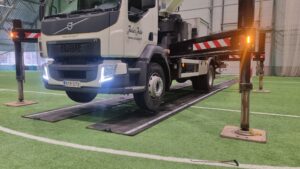 Palloiluhallin sisällä olevan nostolava-auton renkaiden alla on komposiittilevyjä, jotta lattia ei vahingoitu. Autosta näkyy vain alaosa.