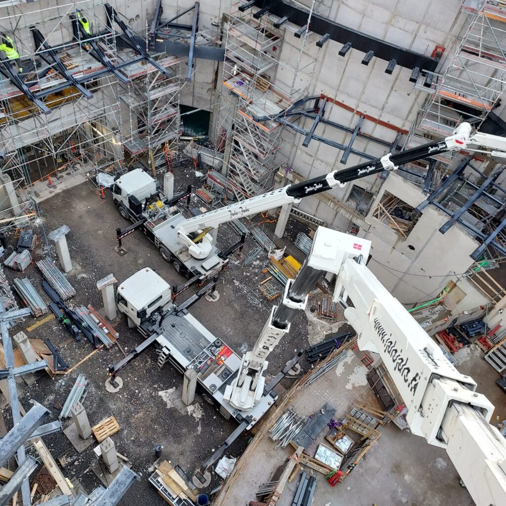 Korkealta otettu sisäkuva konserttitalo Fuugan rakennustyömaalta. Kuvassa näkyy ylhäältä päin kaksi nostolava-autoa, rakennustarvikkeita ja rakentajia.