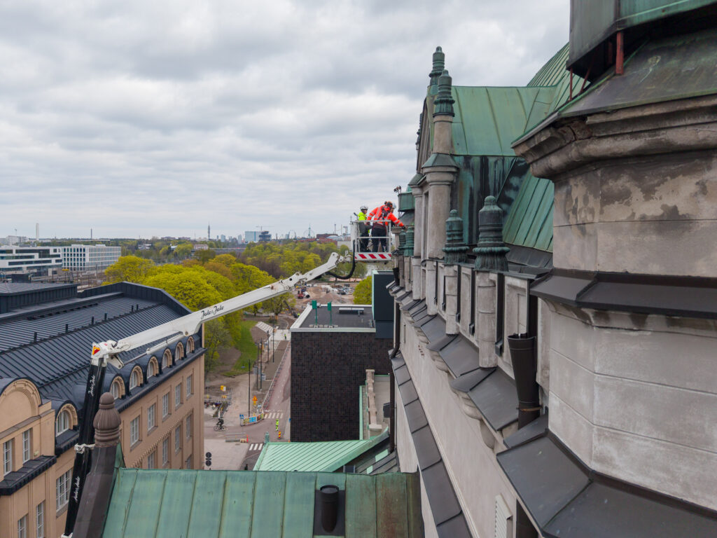 Kansallisteatterin kattoa tutkitaan nostolava-auton korista, taustalla näkyy Helsinkiä